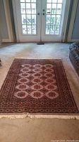 Rectangular wool area rug featuring hexagonal floral motifs placed on a beige carpeted floor near a windowed door.