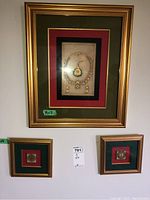 Framed wall art trio hanging on a white wall, green and red matting, gold-tone frames, the largest piece displays a necklace and earrings motif