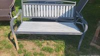 Front and angled views of weathered gray outdoor garden bench sitting on grass with visible wear on the metal frame and wooden slats.