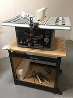 Full view of bench saw mounted on Hirsh stand showing table top, blade guard, stand and accessories on lower shelf