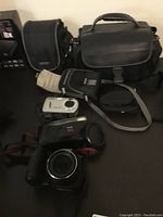 GE video camera and several cameras with lenses and bags on a dark surface