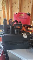 Black & Decker chainsaw on top of a black plastic case with red gas can behind