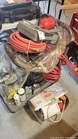 Photo showing coiled red and black air hoses, grey accessory case, and trigger nozzle gun with red container on utility cart.