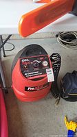 Front left angle of red Pro Air II air compressor showing shape, color, hose, and top handle.