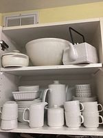 White ceramic coffee set with cups, mugs, sugar bowl, creamer, and various sized ribbed bowls and large mixing bowl on white shelving
