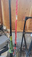 Full view of electric mini chainsaw and manual branch saw with long handles next to each other against a wooden wall.
