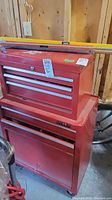 Front view of red metal tool box with three drawers on top chest and larger base with drawer and compartment below. A level rests on top.