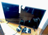 Full view of 40-inch RCA Roku flat-screen TV standing on surface with wall mount and bundled remotes taped with green tape inside frame area.