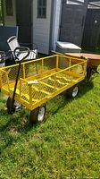 Front and side view of yellow utility wagon showing mesh construction, pneumatic wheels, and pulling handle in grass outside.