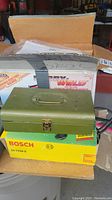 Open cardboard box containing Lincoln Electric Hobby Welder box, Bosch angle grinder box, and green metal torch case with handle and attached cables
