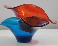 Side view of two art glass bowls: one bright orange, one bright blue, fitted together with flowing, curved edges.