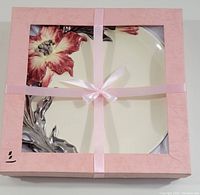Plate in pink box tied with ribbon, showing partial floral decoration through window