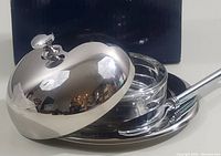 Butter dish set with polished stainless steel dome lid, wide stainless steel base, clear glass bottom dish, and stainless steel spreader placed on the base.