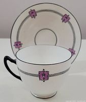 Close-up photo of Paragon Star bone china cup with Art Deco design featuring a chain-like black band and pale purple square motifs. The cup has a black handle and a black rim line. Saucer visible behind the cup with matching decorative elements.