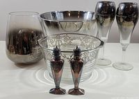Photo of 7 decorative items: glass bowl with etched floral pattern, small silver-tone bowl, two smoked gradient vases, and a pair of red glass salt and pepper shakers.