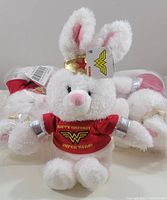Four white plush bunny toys with pink nose and ears, wearing red 'Happy Birthday Superhero' shirts with Wonder Woman logo, showing new condition and tags.