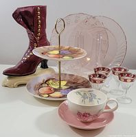 Photo showing all items: ceramic boot figurine, pink glass plates, two-tier fruit plate stand, cordial glasses, and floral teacup with saucer.