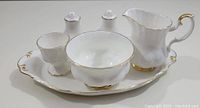 Setup of all six items showing tray, creamer, salt and pepper shakers, open sugar bowl, egg cup with gold trim on white porcelain.