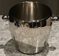 Polished stainless steel ice bucket with round handles, reflective finish on granite countertop