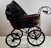 Side view of vintage antique style miniature carriage showing wicker basket, metal wheels, and black fabric canopy.