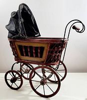 Side angled view of vintage antique style carriage showing woven basket design, black fabric canopy, wooden handle, and spoked wheels.