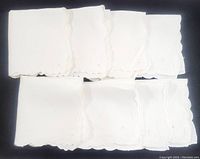 Eight white vintage linen dinner napkins laid out, showing scalloped and embroidered edges.