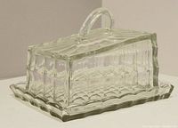 Side view of vintage pressed glass lidded cheese dish showing rectangular lid with thumbprint pattern and scalloped edge base plate