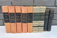 Nine antique hardcover books displayed upright against a grey brick wall, including five volumes of Winston Churchill's WWII series with orange cloth covers, two volumes of W. Somerset Maugham short stories in beige cloth, and two Kathleen Norris novels in dark cloth.
