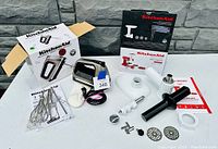 Wide view of all items in lot including kitchen grinder, blender, multiple accessories, and original boxes on white table against a stone wall.