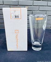 Photo showing the Nachtmann Nova art glass vase next to its original white box with orange branding and label, vase is clear with a tapering cylindrical shape and thick base