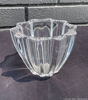 Side view of a thick, clear pleated glass bowl highlighting its scalloped rim and vertical pleats.