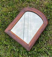 Small antique mirror laying on grass showing wood grain frame and arched shape