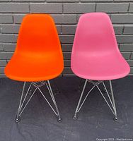 Front view of small orange and pink Vitra Eames chairs with plastic seats and chrome Eiffel-style wire bases