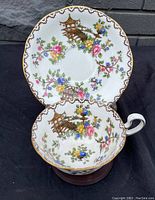 Porcelain teacup and saucer showing floral and gold pagoda bridge pattern, displayed on stand.