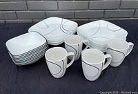 Full set containing plates, bowls, and mugs arranged on black surface in front of gray brick wall.