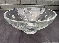 Angled side view of the clear crystal glass bowl showing the etched floral and leaf pattern around the outside and the bowl's shape and thickness.