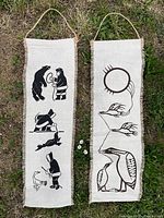 Both Inuit art tapestries hung on grass showing full length and artwork details.