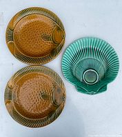 Two brown fish-shaped plates and one turquoise seashell-shaped plate laid out side by side showing top view and glaze details.