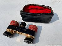 Photo of vintage Eikow opera glasses with red textured grips next to fitted black leather zippered case lined in red.