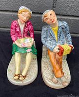 Front view of pair of antique Wedgwood figurine bookends showing seated man holding concertina and seated woman holding flowers.