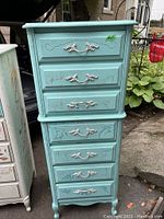 Side-view photo of the light blue vintage chest on chest dresser showing six drawers with silver handles, paint scribbles, and signs of wear.