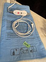 Full view of blue heat pad with attached control unit and coiled power cord. Shows fabric surface and overall condition plus safety printing.