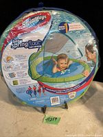 Photo of original SwimWays Baby Spring Float Sun Canopy in its packaging showing product details and infant using float under sun canopy