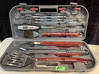 Complete BBQ cutlery set displayed in open grey plastic carrying case, showing all 12 pieces arranged in molded compartments.