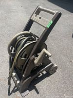 Front angle of a dark brown and beige plastic hose reel with a black and yellow garden hose coiled on it, showing the handle and crank.