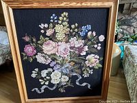 Front view of large needlepoint floral wall art in wood frame with variety of colorful flowers on black background.
