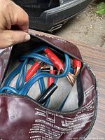 Blue jumper cables with red and black insulated clamp handles inside maroon vinyl carrying case.
