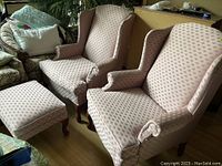 Pair of salmon pink wingback chairs and matching foot stool arranged on wooden floor, showing fabric pattern and Queen Anne cabriole legs