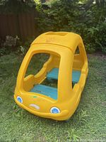 Photo showing the front and side view of the yellow Step 2 toddler bed shaped like a car with blue interior platform and face stickers on the front.
