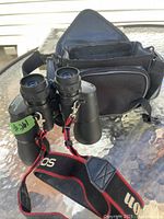 Tasco binoculars sitting on glass table with carrying case behind. Neck strap attached.